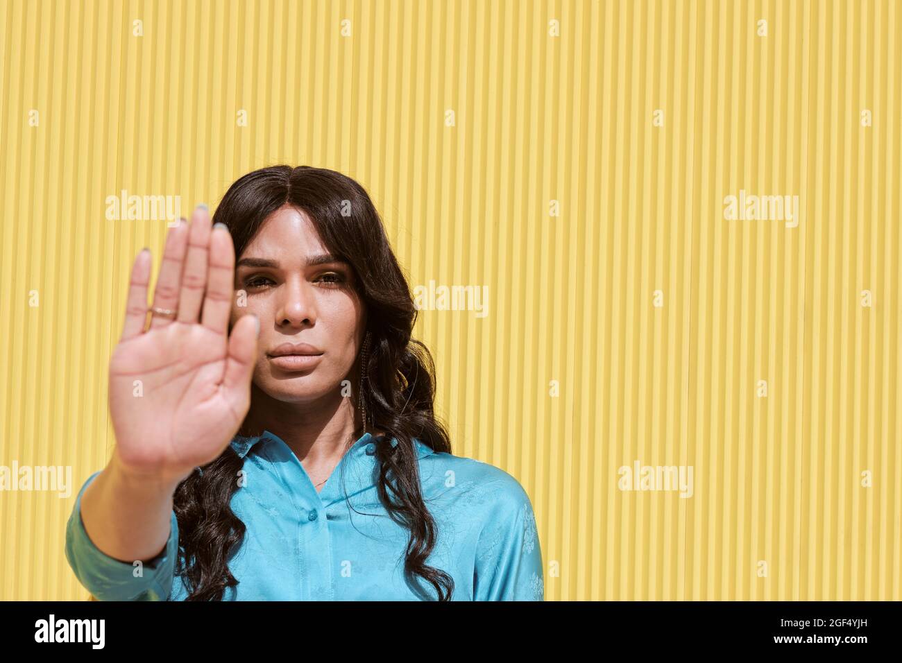 Nicht-binäre Frau mit Stop-Geste vor der gelben Wand Stockfoto