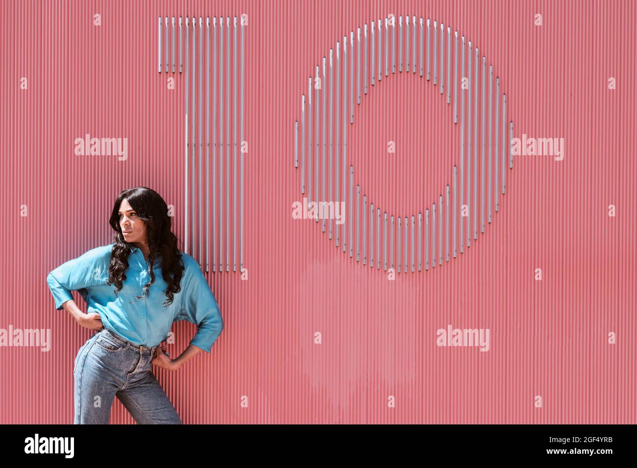Selbstbewusste weibliche Transgender-Frau, die mit Nummer 10 auf der rosa Wand wegschaut Stockfoto
