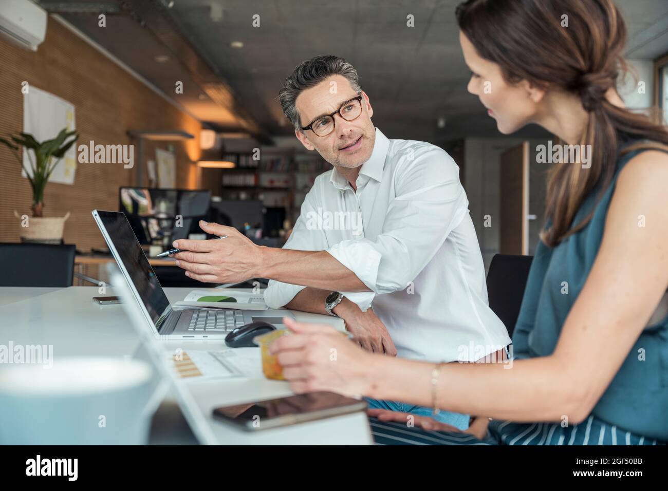 Ein Geschäftsmann erklärt dem Kollegen, während er am Arbeitsplatz sitzt Stockfoto