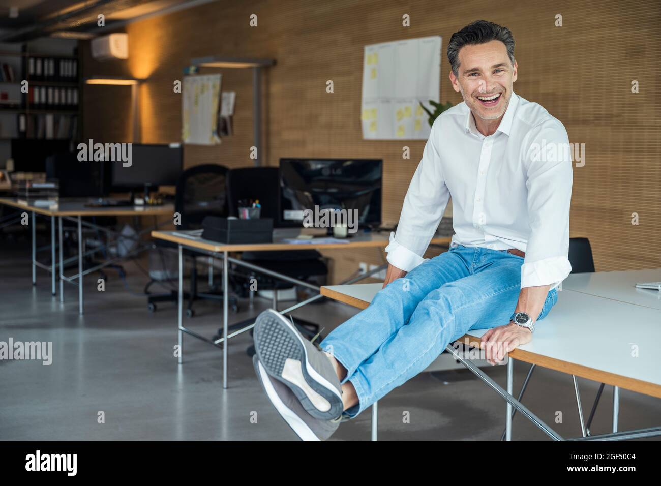 Fröhlicher Geschäftsmann mit gekreuzten Beinen am Knöchel auf dem Schreibtisch Stockfoto