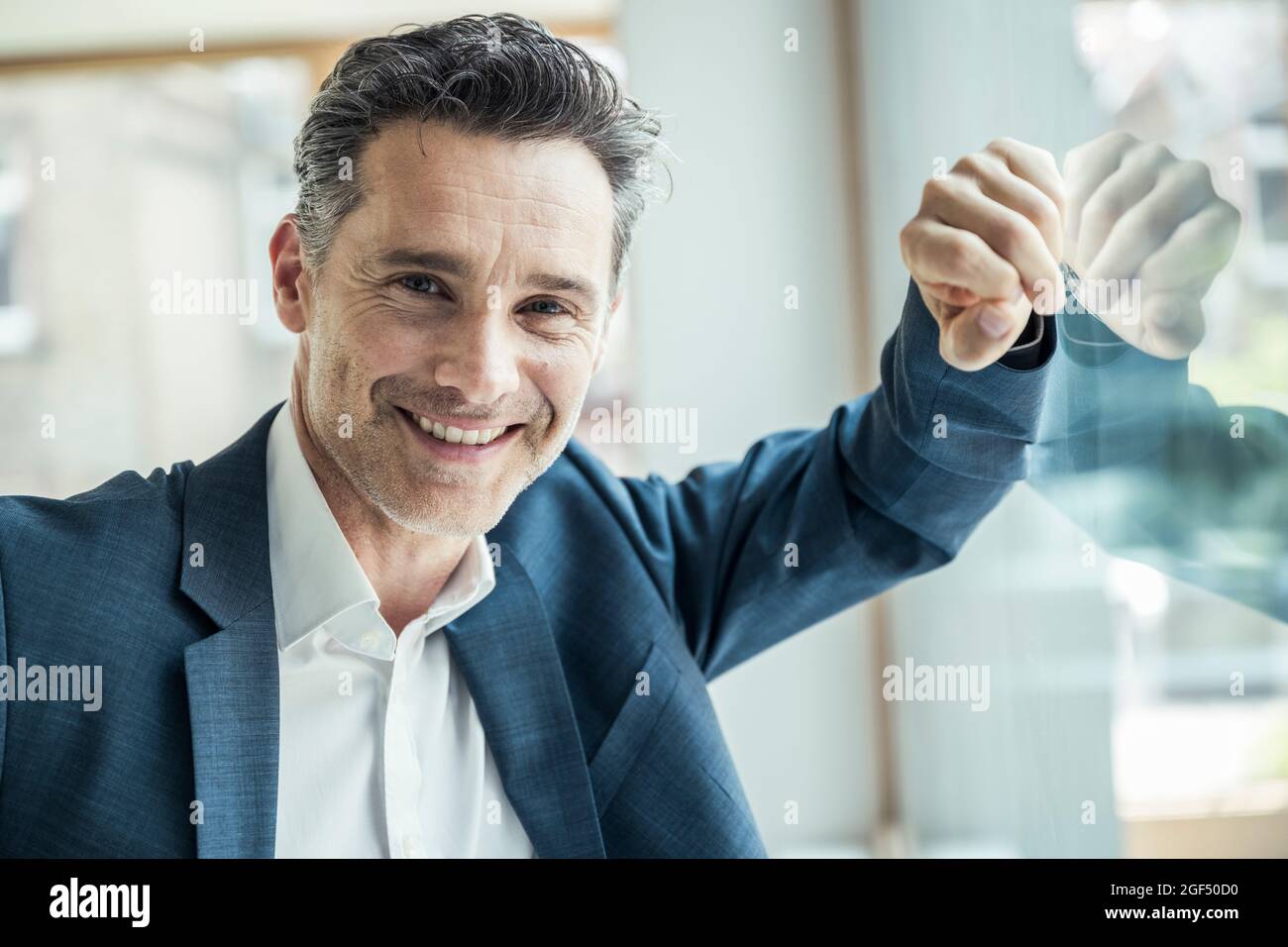 Lächelnder Geschäftsmann, der sich an das Bürofenster lehnt Stockfoto