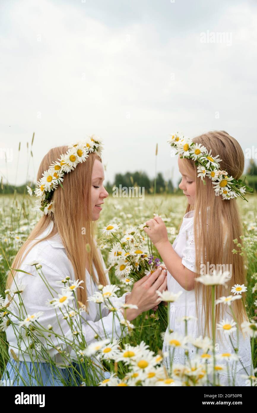 Blonde Frau trägt Blume Tiaras sammeln Blume mit Mädchen auf dem Feld Stockfoto