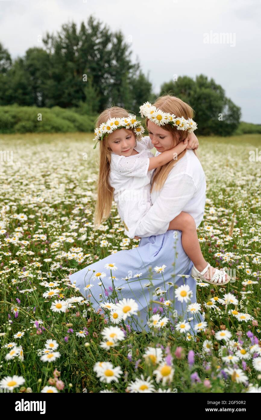 Frau mit Blumen-Tiaras, die Tochter beim Gehen auf dem Kamillenfeld tragen Stockfoto