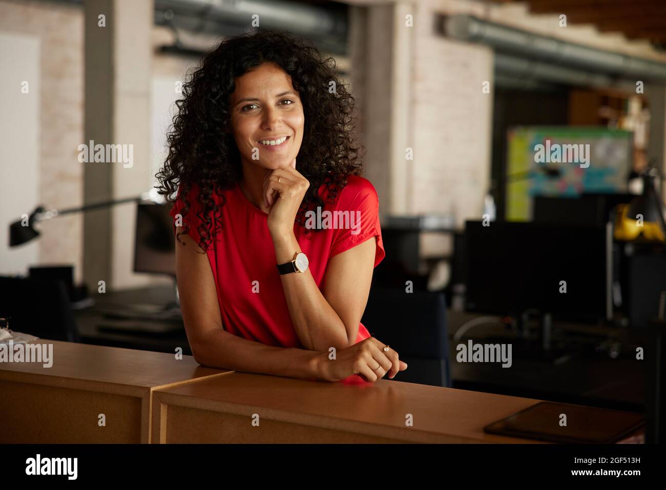 Lächelnde Geschäftsfrau mit der Hand auf dem Kinn am Arbeitsplatz Stockfoto