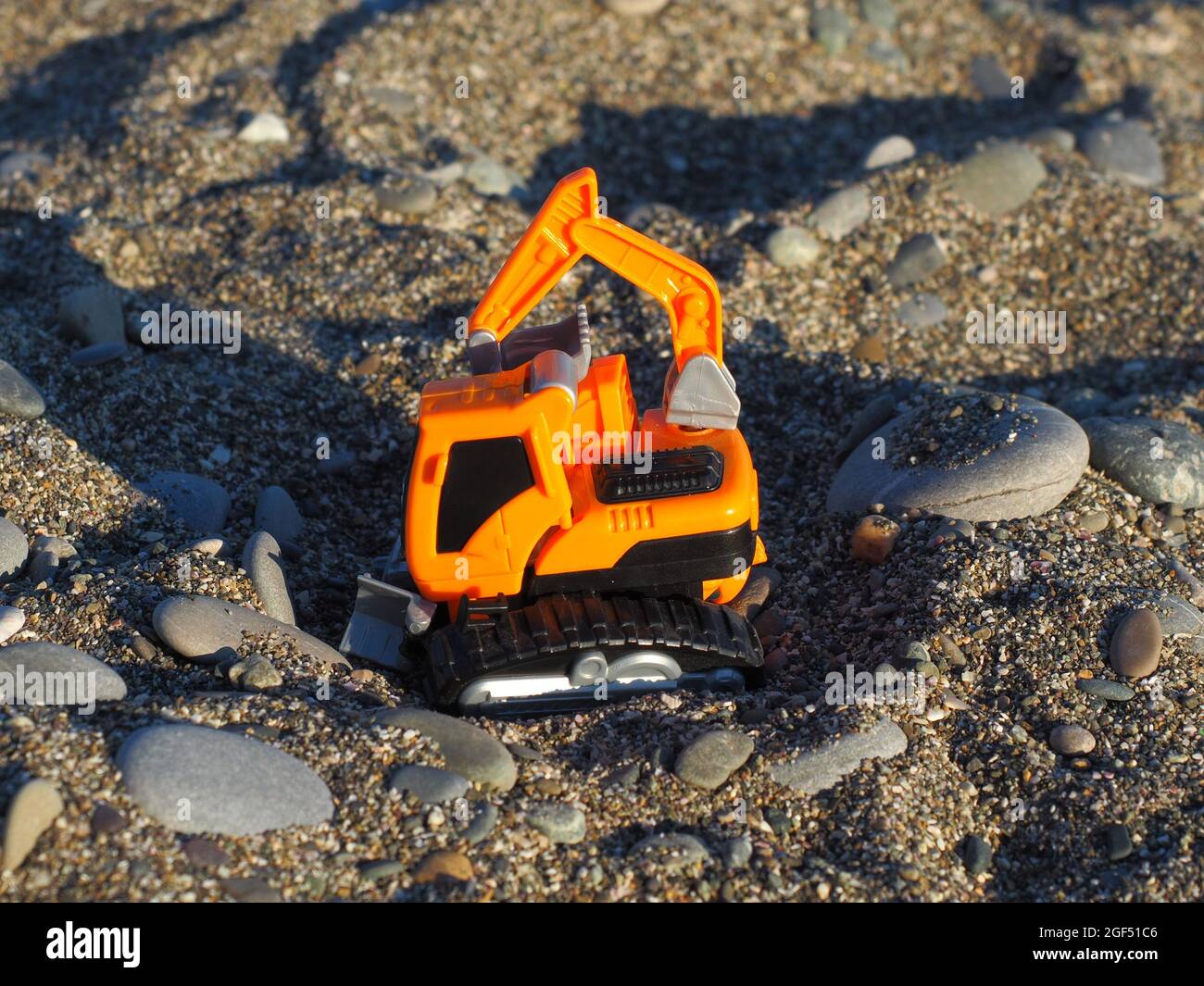 Spielzeug orange Traktor auf grobem Sand mit Kieselsteinen von der Sonne beleuchtet Stockfoto