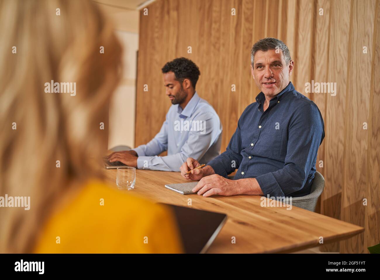 Ein männlicher Fachmann, der mit einer Kollegin spricht, während er im Vorstandszimmer von einem Geschäftsmann sitzt Stockfoto