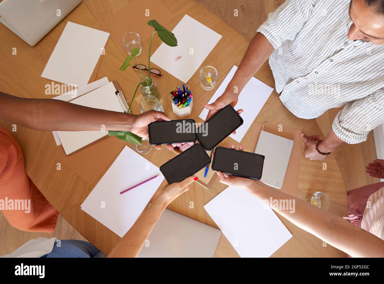 Im Büro halten Männer und Frauen Smartphones über dem Schreibtisch Stockfoto