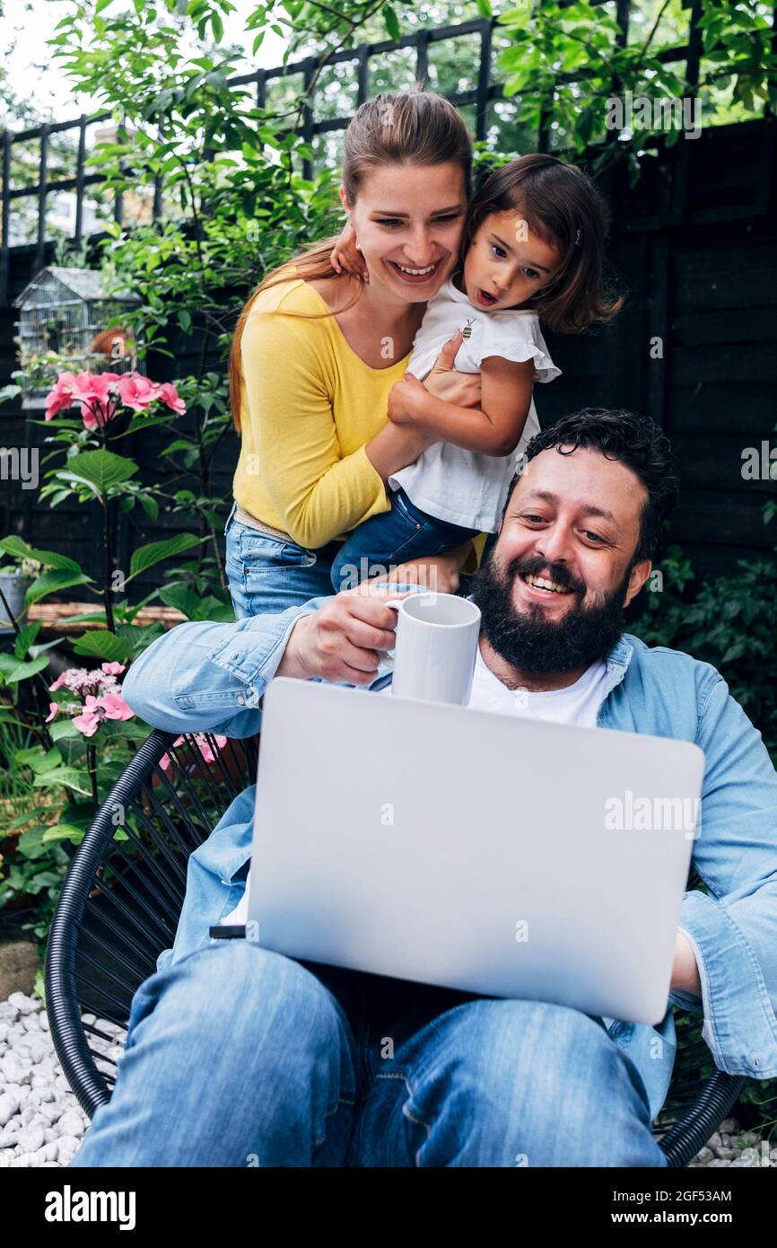 Lächelnde Familie, die über einen Laptop im Hinterhof an einem Videoanruf teilnahm Stockfoto
