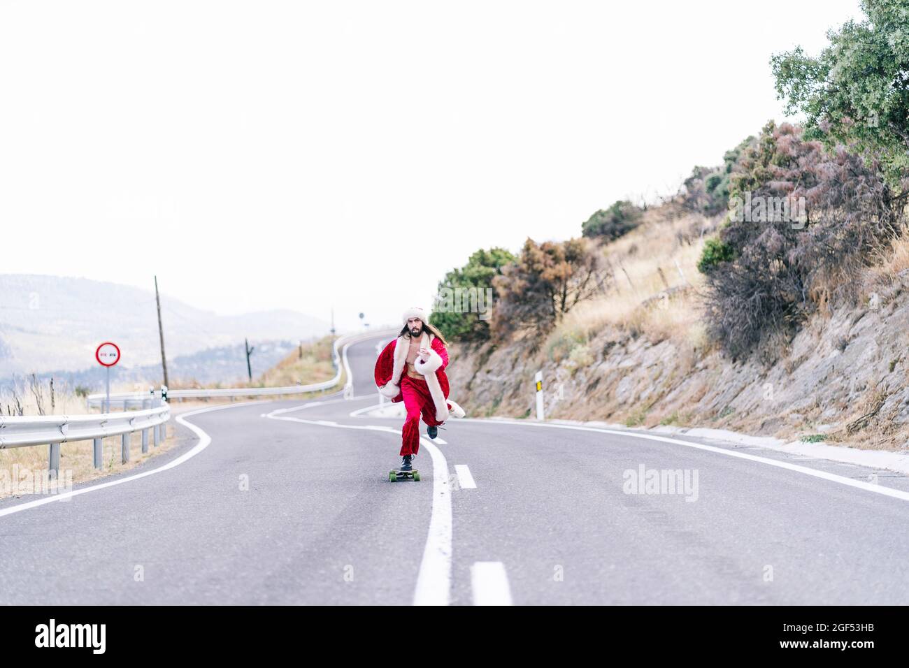 Junger Mann im Santa Claus Kostüm Skateboarding auf der Straße Stockfoto