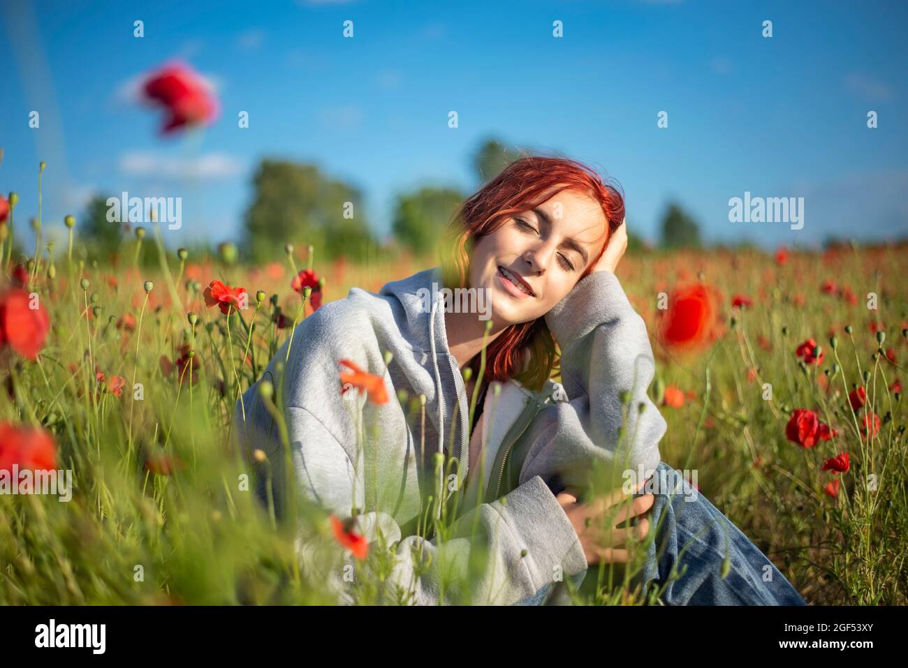 Rotschopf Teenager Mädchen sitzen mit geschlossenen Augen in Mohn Feld an sonnigen Tag Stockfoto