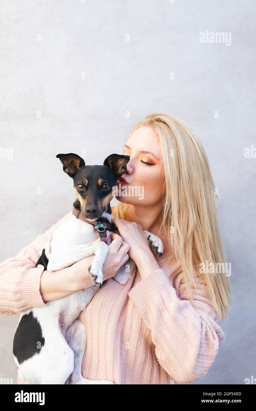 Junge blonde Frau küsst Hund vor der Wand Stockfoto