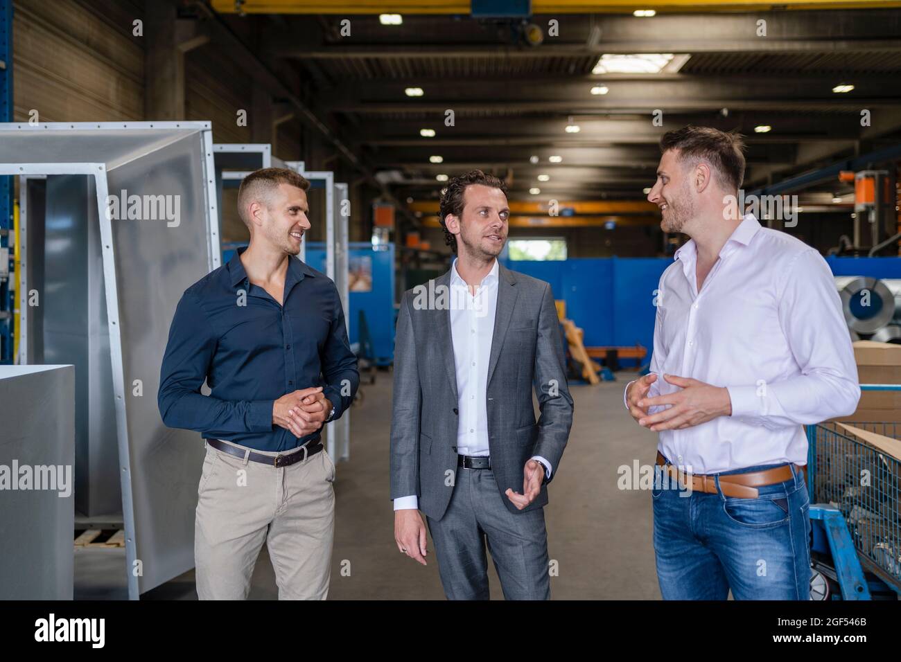 Lächelnde männliche Profis, die in der Fabrik diskutieren Stockfoto