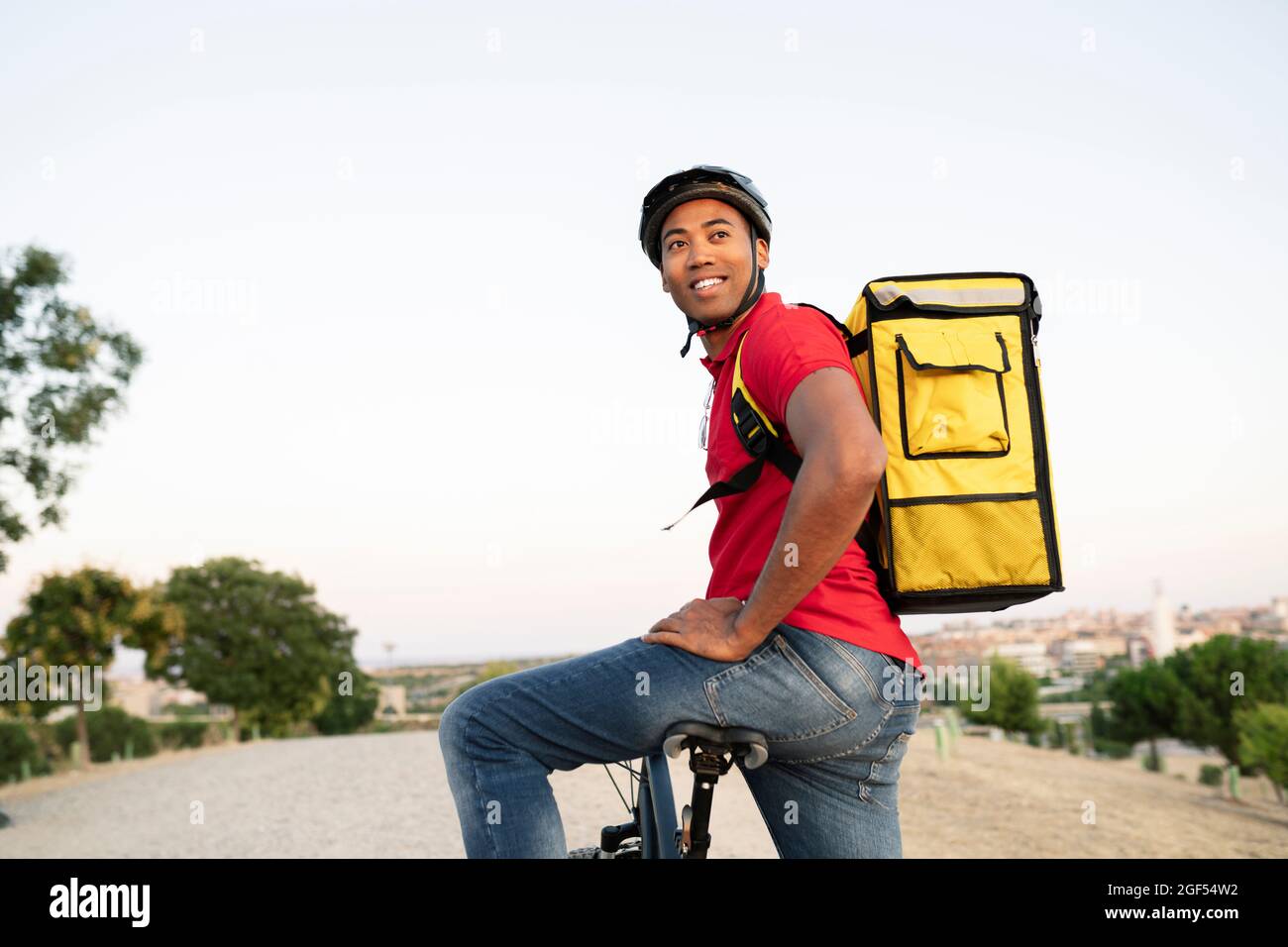 Lächelnder männlicher Entlieferer schaut weg, während er auf dem Fahrrad sitzt Stockfoto