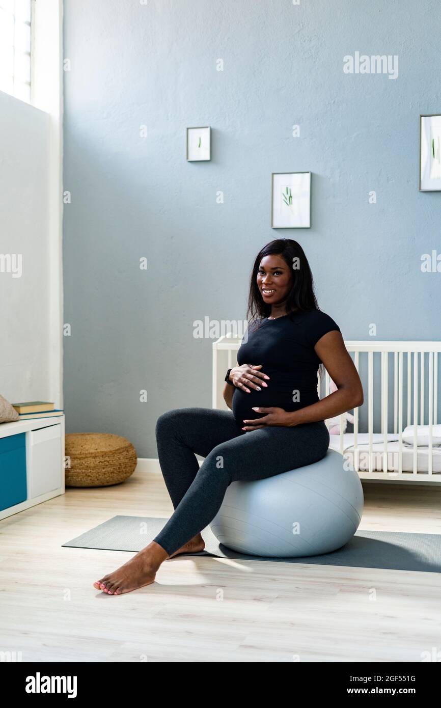 Glückliche, schwanger junge Frau, die zu Hause auf dem Fitnessball sitzt Stockfoto