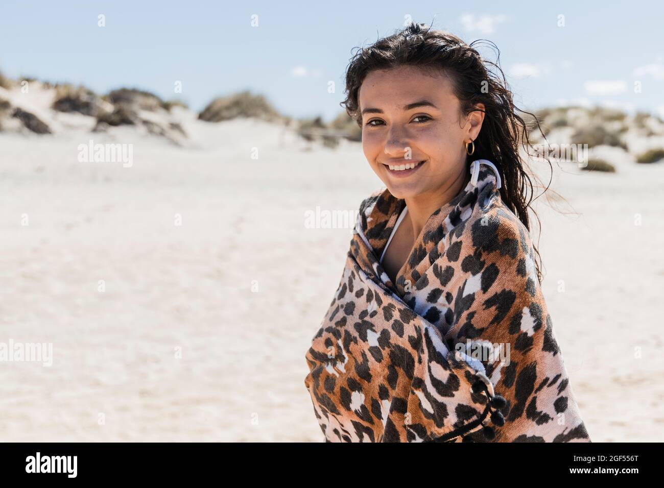 Schöne lächelnde Frau in Schal gewickelt stehen am Strand an sonnigen Tag Stockfoto