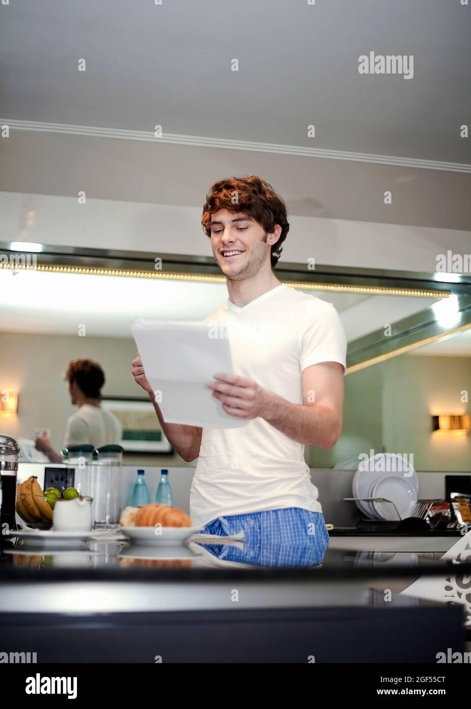Lächelnder junger Mann, der den Brief liest, während er in der Küche steht Stockfoto