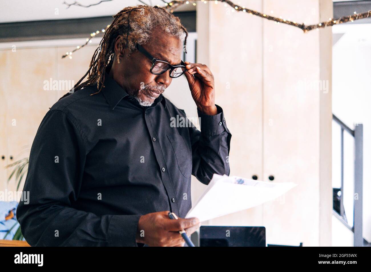 Älterer männlicher Profi, der zu Hause eine Brille hält, während er das Dokument liest Stockfoto