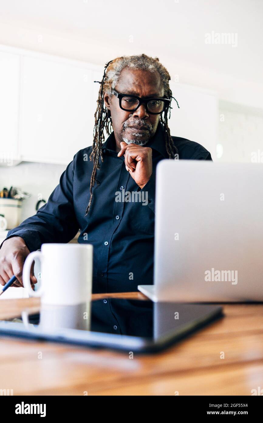 Leitender männlicher Profi, der im Heimbüro einen Laptop betrachtet Stockfoto
