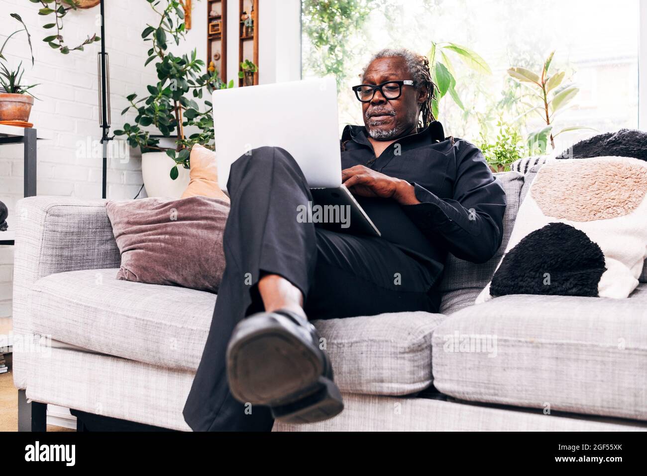 Älterer männlicher Profi, der zu Hause auf dem Sofa sitzt und einen Laptop benutzt Stockfoto