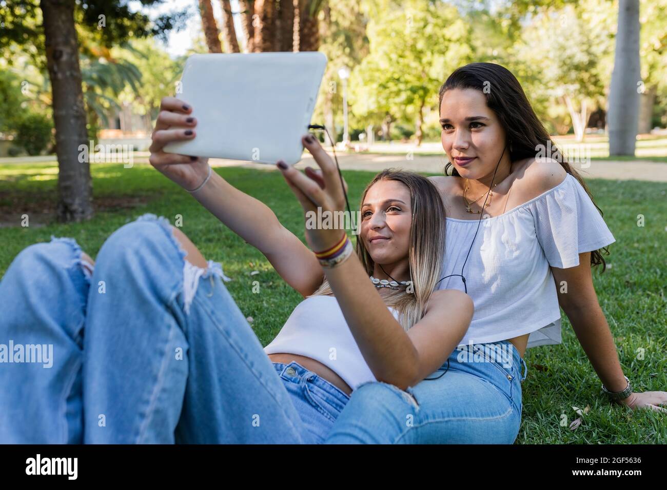 Junge Frau mit einer Freundin, die im Park Selfie über ein digitales Tablet nimmt Stockfoto