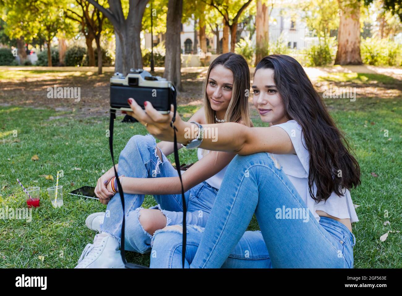 Frauen machen Selfie durch die Kamera, während sie im öffentlichen Park sitzen Stockfoto