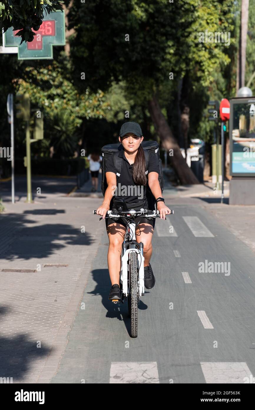 Junge, wichtige Servicearbeiterin, die an sonnigen Tagen Fahrrad auf der Straße fährt Stockfoto