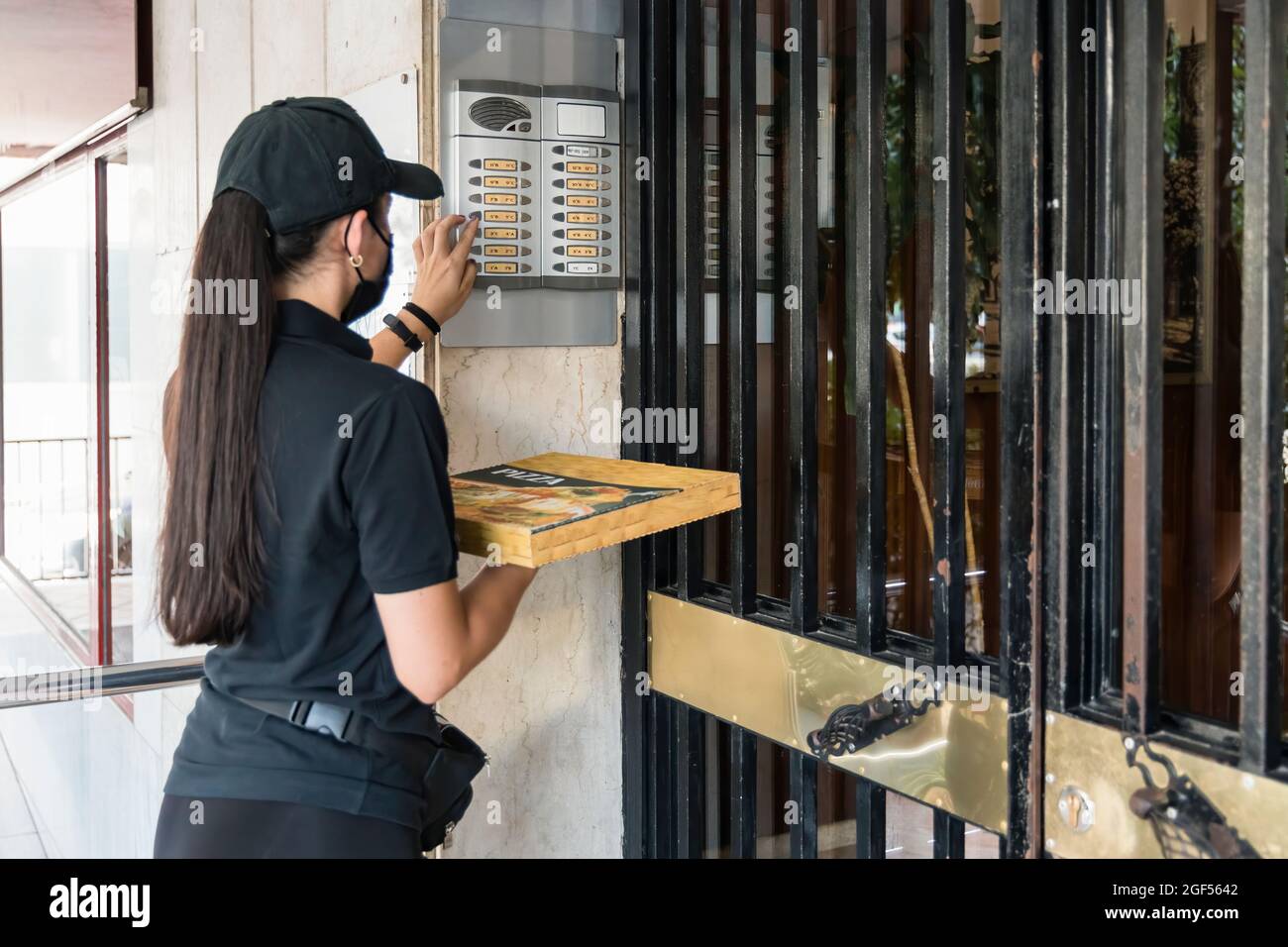 Weibliche Pizza-Lieferperson klingelt während des COVID-19 an der Tür Stockfoto