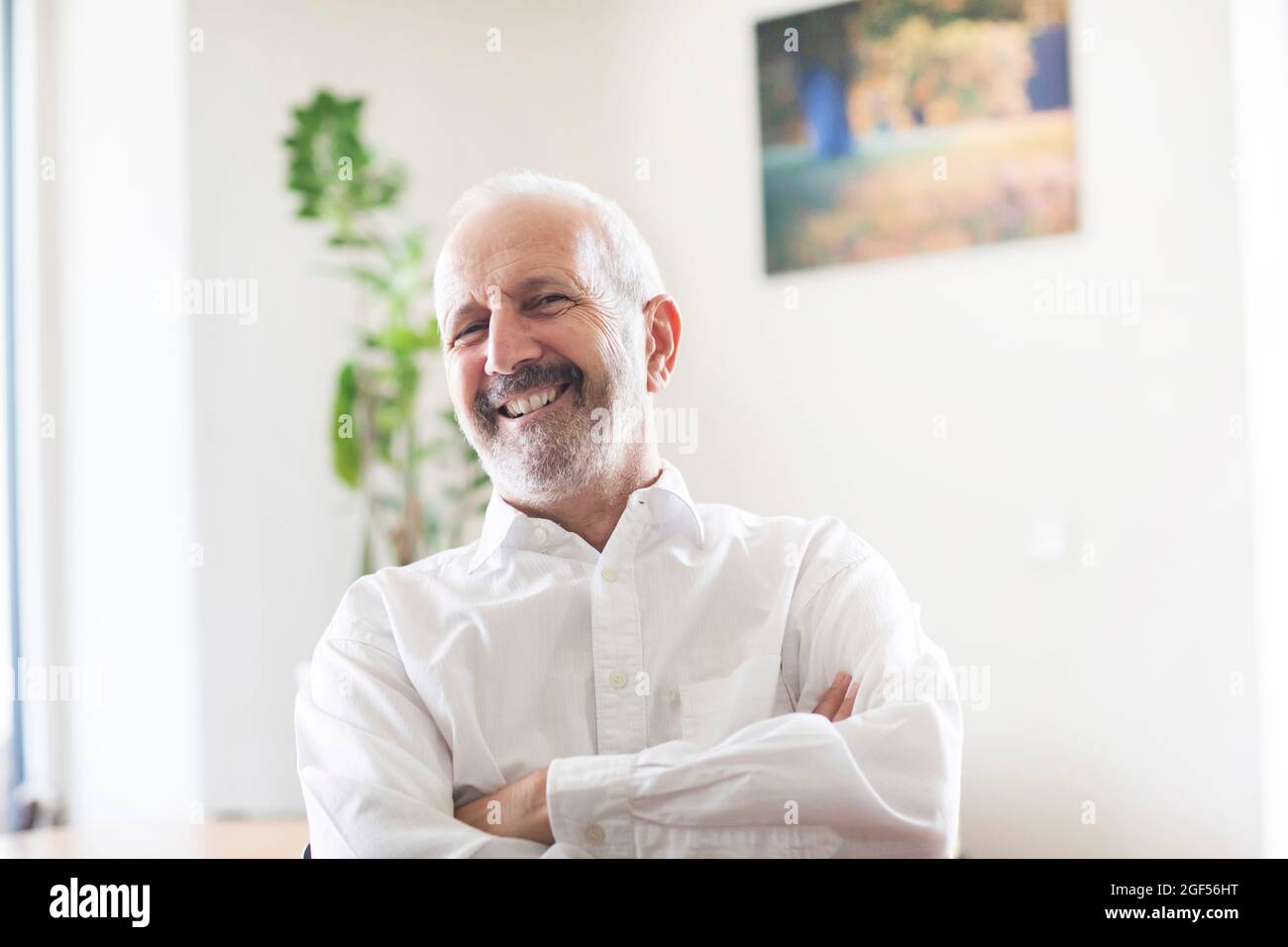 Ein älterer, männlicher Profi lächelt mit gekreuzten Armen im Büro Stockfoto