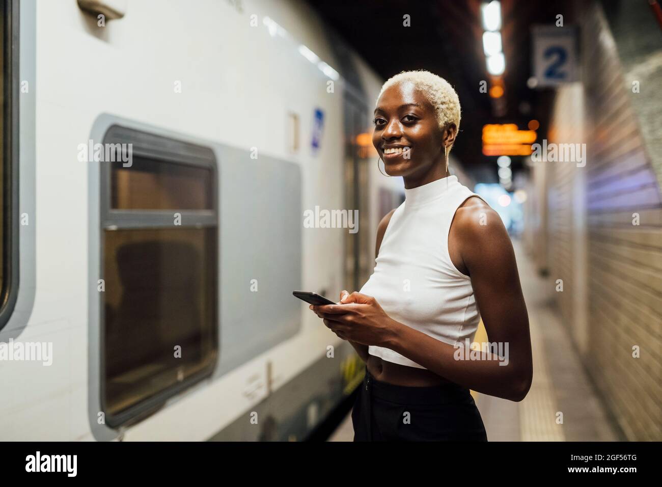 Lächelnde Frau mit Mobiltelefon, während sie an der U-Bahn-Station stand Stockfoto