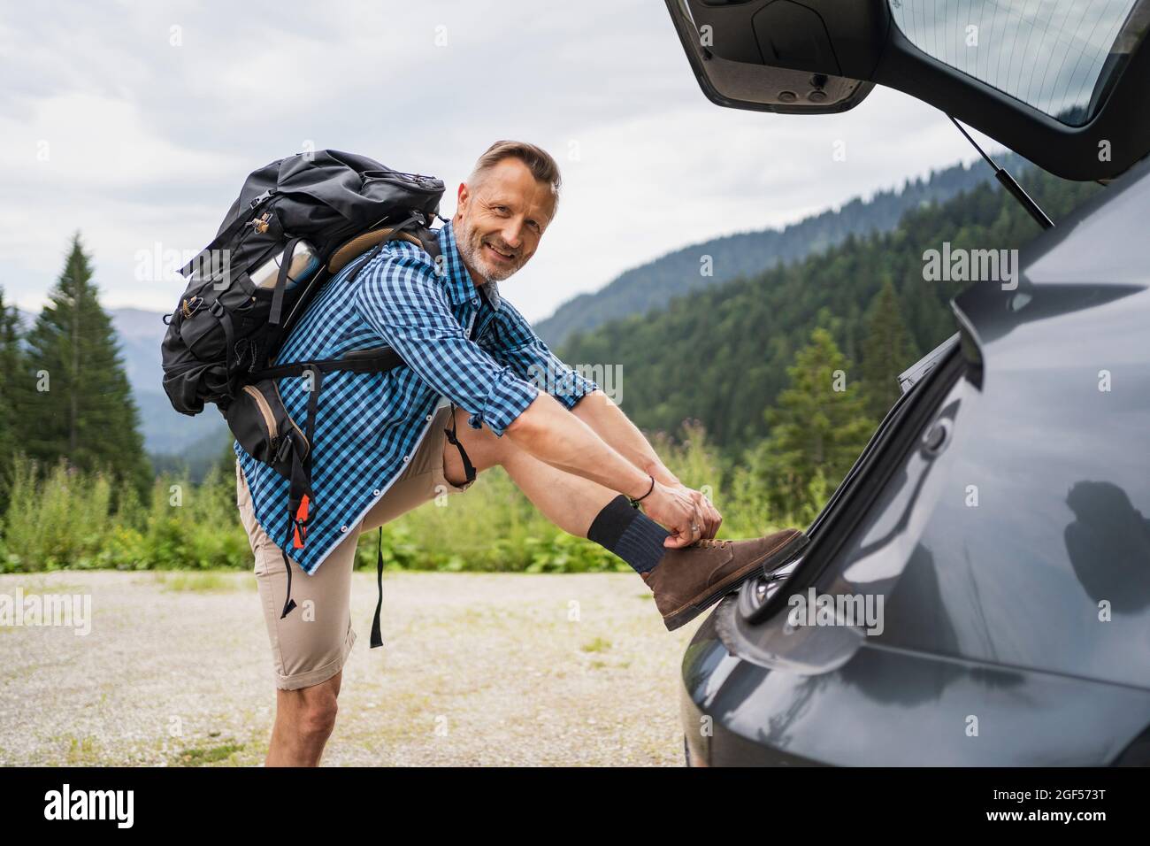 Männlicher Rucksacktourist, der sich auf den Kofferraum lehnte und dabei Schnürsenkel festBand Stockfoto
