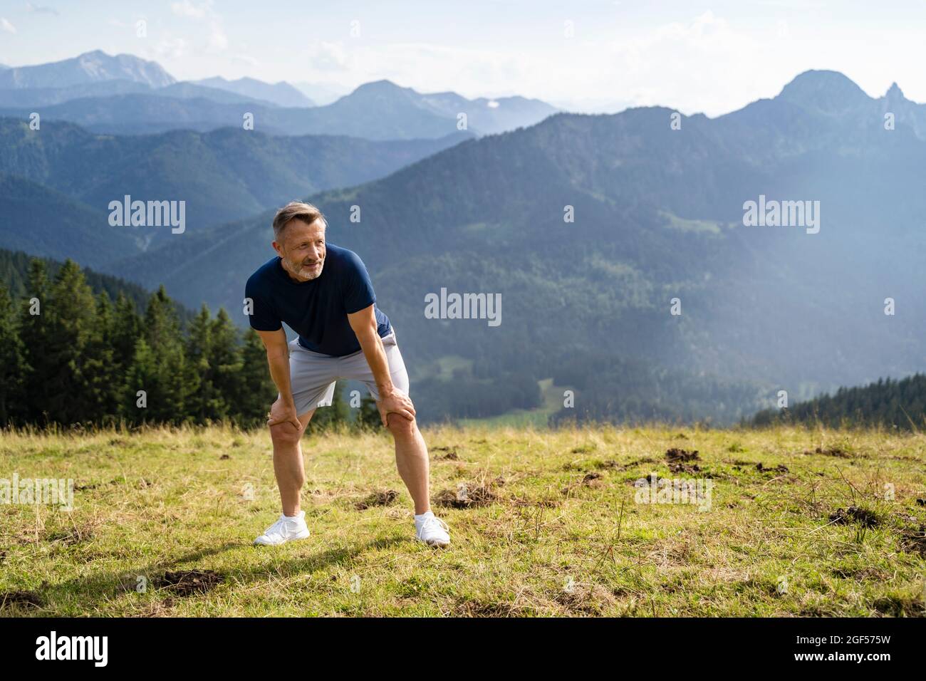 Müde Mann mit den Händen auf den Knien am Berg an sonnigen Tagen Stockfoto