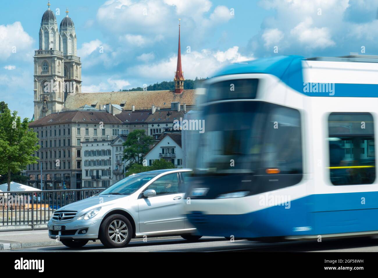 Zürich, Schweiz - 13. Juli 2019: Eine Straßenbahn überholen ein wartender Wagen vor der Grossmünster-Kirche Stockfoto