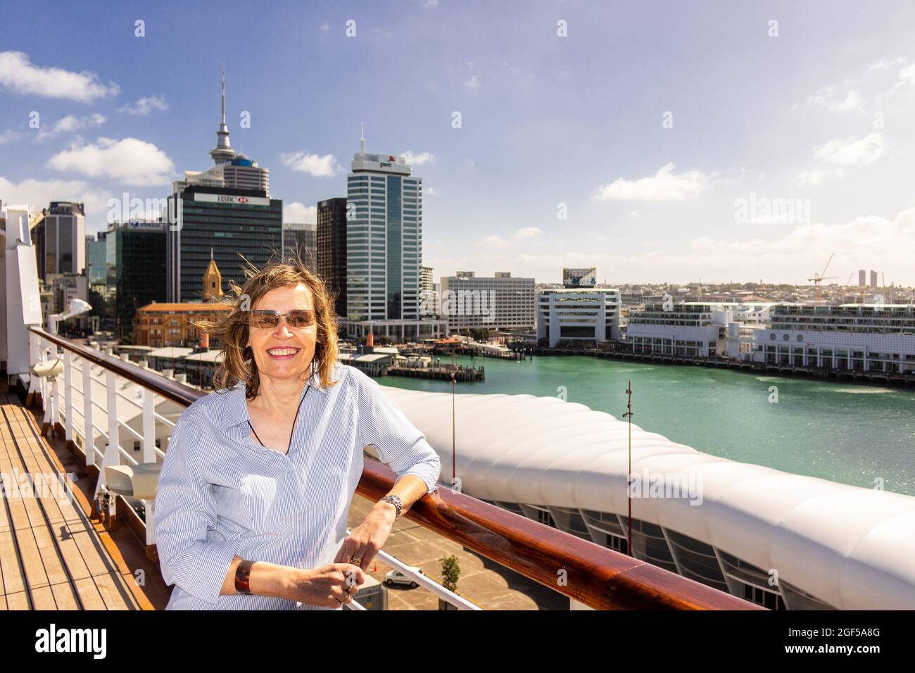 Kaukasische Frau mittleren Alters, die auf dem Deck eines Kreuzfahrtschiffs steht, das den Kreuzfahrthafen von Auckland, Neuseeland, verlässt Stockfoto