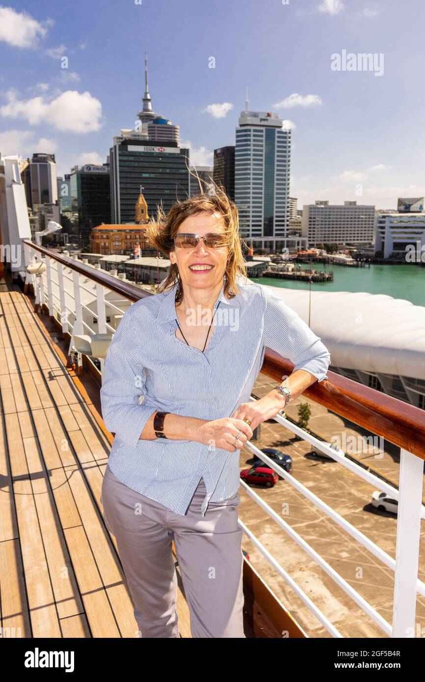 Kaukasische Frau mittleren Alters, die auf dem Deck eines Kreuzfahrtschiffs steht, das den Kreuzfahrthafen von Auckland, Neuseeland, verlässt Stockfoto