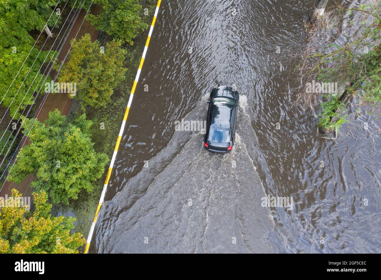 Überflutete Straße nach einem ungewöhnlichen Regenguss in den Vororten. Autos bewegen sich auf der überfluteten Straße. Folgen einer Naturkatastrophe. Stockfoto