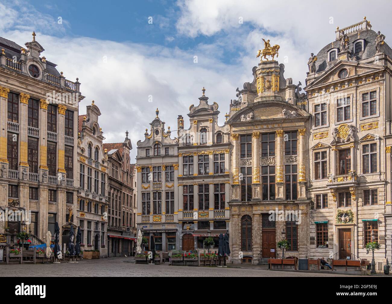 Brüssel, Belgien - 31. Juli 2021: Fassaden historischer Gildenhäuser auf der SW-Seite des Grand Place unter blauer Wolkenlandschaft. Goldene Statuen und Ornamente. Stockfoto