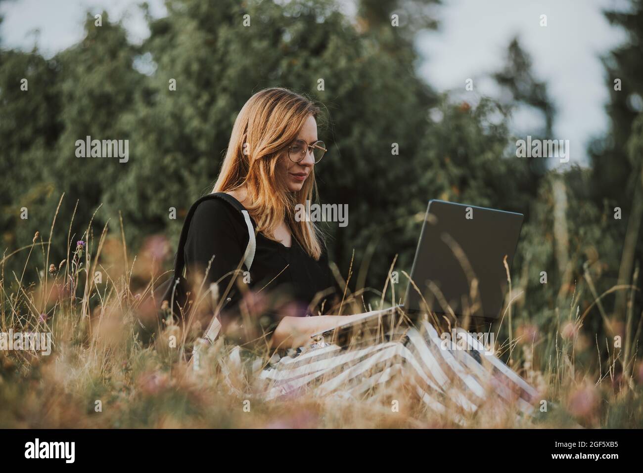 Glückliche Freiberuflerin mit Brille, die am Laptop arbeitet, abgelegene Lage in der Natur Stockfoto