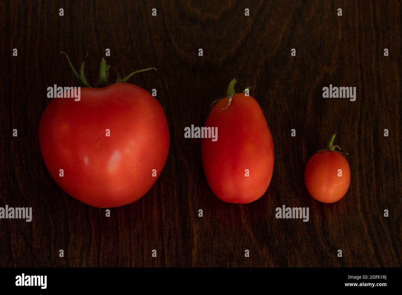 Seitenansicht von drei Tomaten unterschiedlicher Größe auf Holzhintergrund Stockfoto