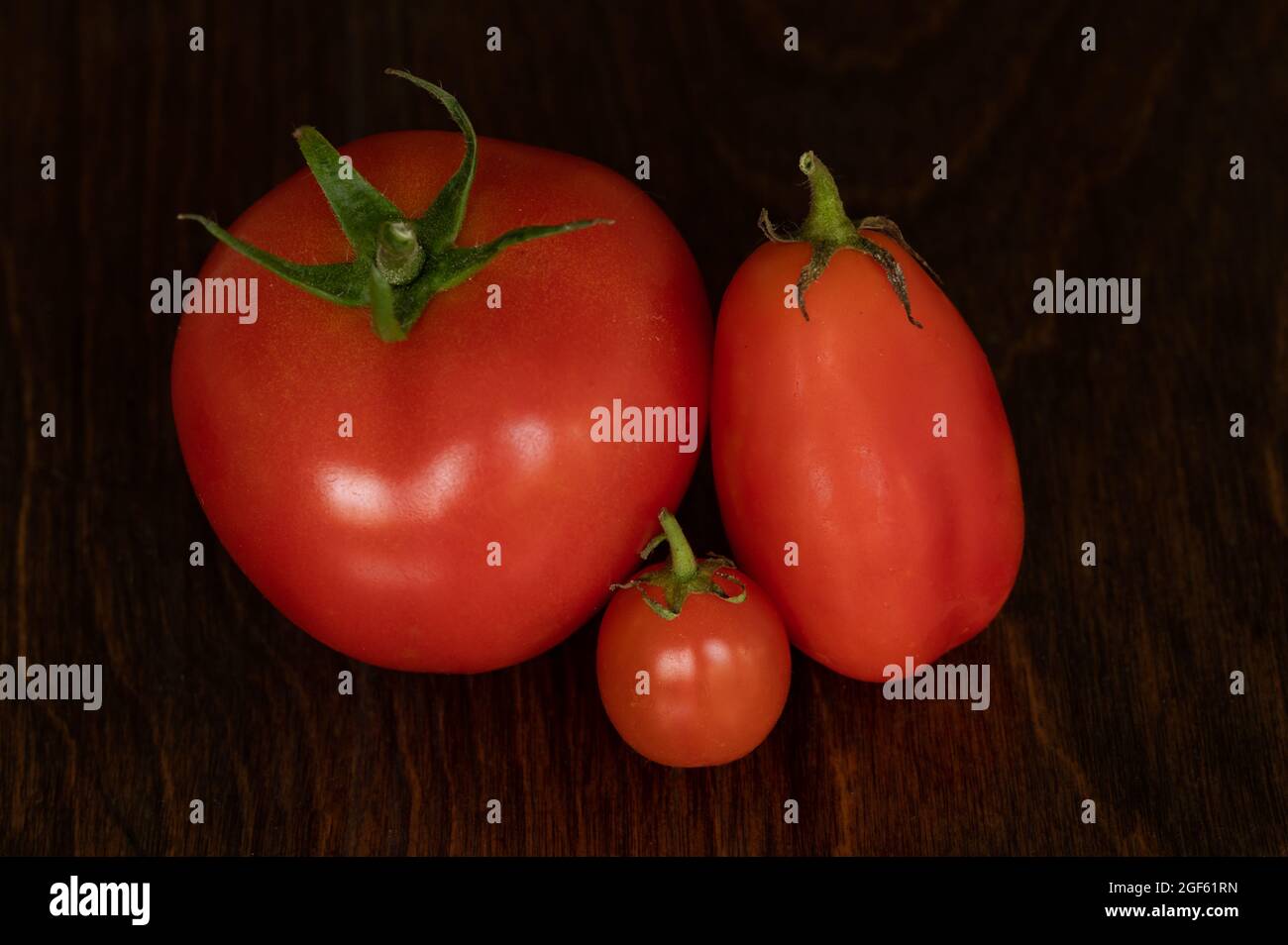 Draufsicht auf drei Tomaten in verschiedenen Größen auf Holzhintergrund Stockfoto