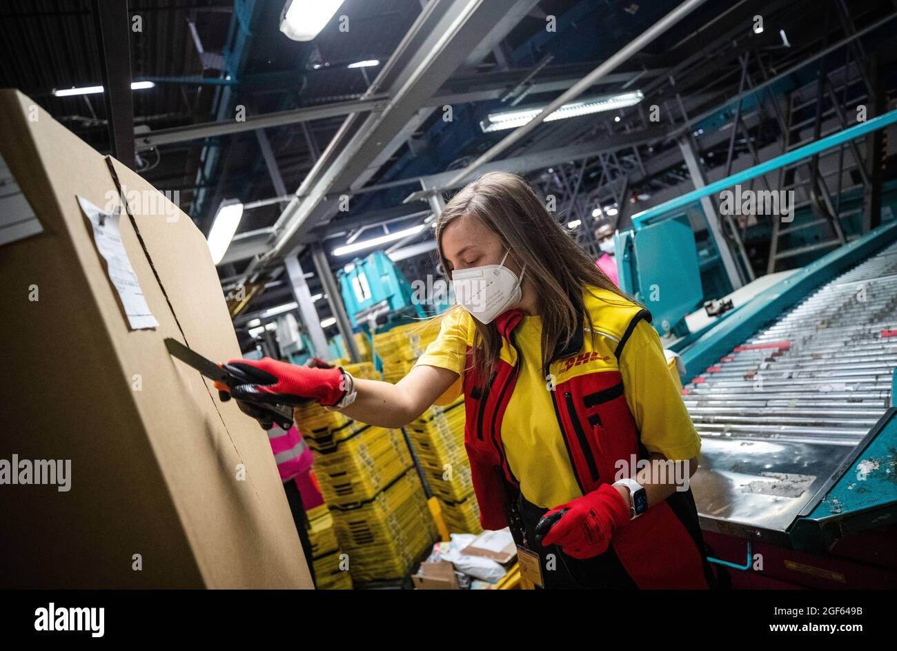 19. August 2021, Baden-Württemberg, Köngen: Adriana Tec, Dispatcher im DHL Paketzentrum in Köngen, schneidet während ihrer Nachtschicht einen großen Container auf, um nachfolgende Pakete auf eine Montagelinie zu legen. (An dpa: 'Hohes Paketvolumen im DHL-Distributionszentrum - Corona oder nicht') Foto: Christoph Schmidt/dpa Stockfoto
