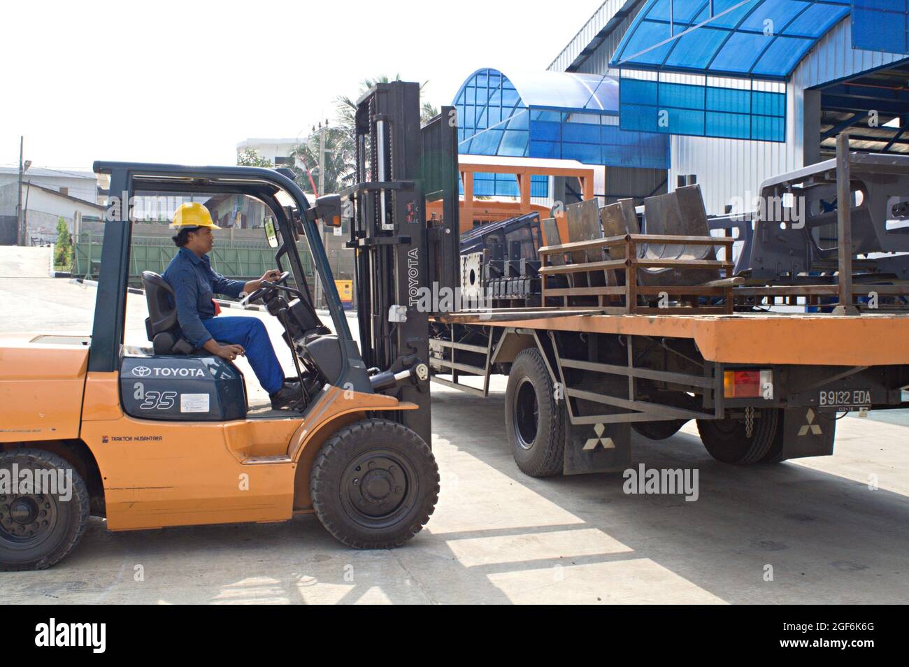 Ein Arbeiter setzt einen Gabelstapler ein, um einige Metallrahmen auf einen Lkw zu setzen. Stockfoto