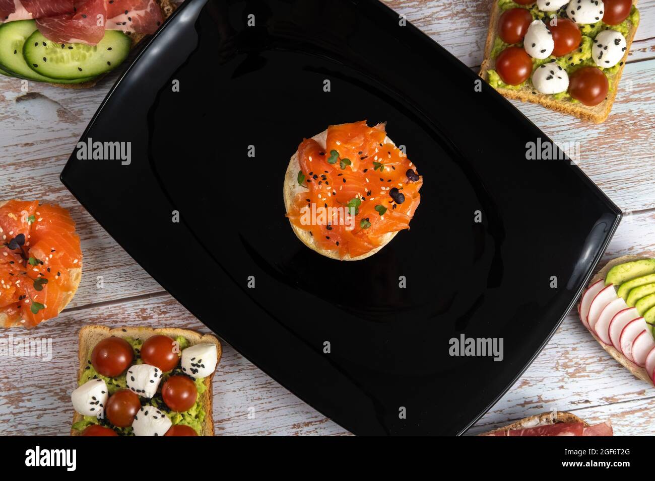 Ein Sandwich mit rotem Fisch befindet sich auf einem schwarzen Teller und es gibt viele andere Sandwiches. Stockfoto