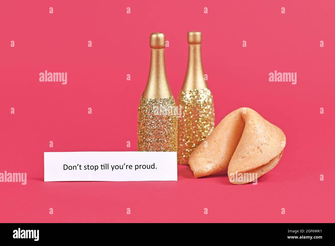 Glückskekekieschen und Champagnerflaschen mit dem Motivationstext „Don't stop until you're stolze“ auf Papier auf rosa Hintergrund Stockfoto
