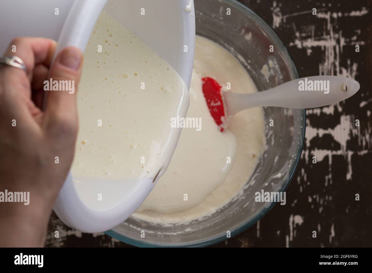 Draufsicht der Frau, die von Hand geschwollene Eier in geschwollenen Grießteig als Zutat zum Backen von Mannikusszärteln auf braunem Hintergrund gießt Stockfoto