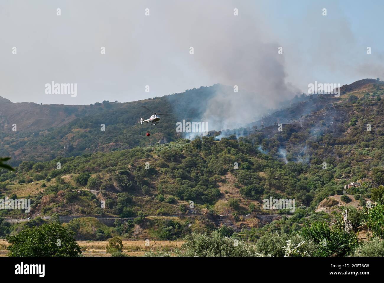 Feuern Sie einen Hubschrauber, der Wasser aus einem Eimer auf ein Waldfeuer in den Bergen ablässt. Waldbrände sind eine Umweltkatastrophe. Entwaldung. Stockfoto