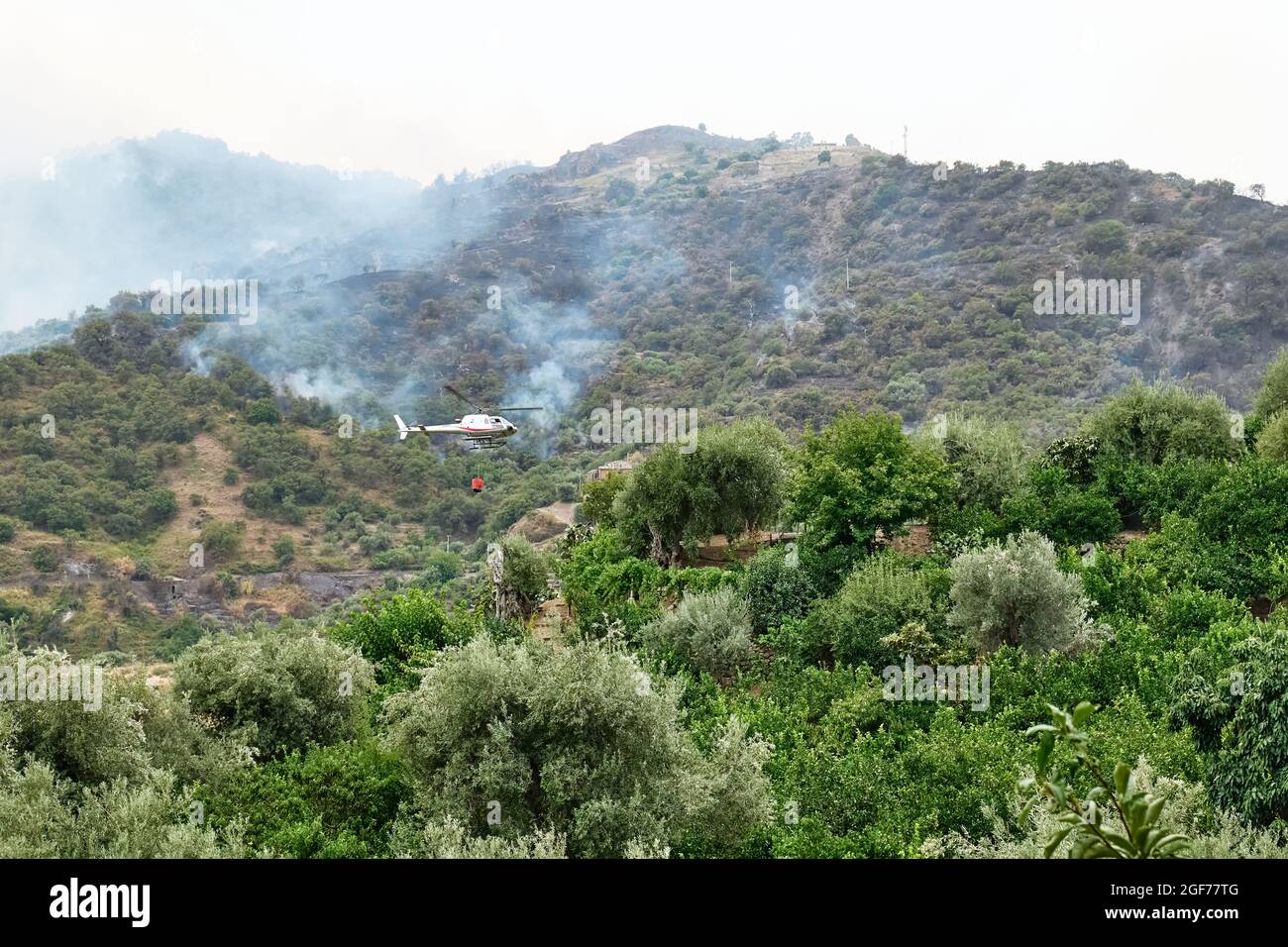 Feuern Sie einen Hubschrauber, der Wasser aus einem Eimer auf ein Waldfeuer in den Bergen ablässt. Waldbrände sind eine Umweltkatastrophe. Entwaldung. Stockfoto