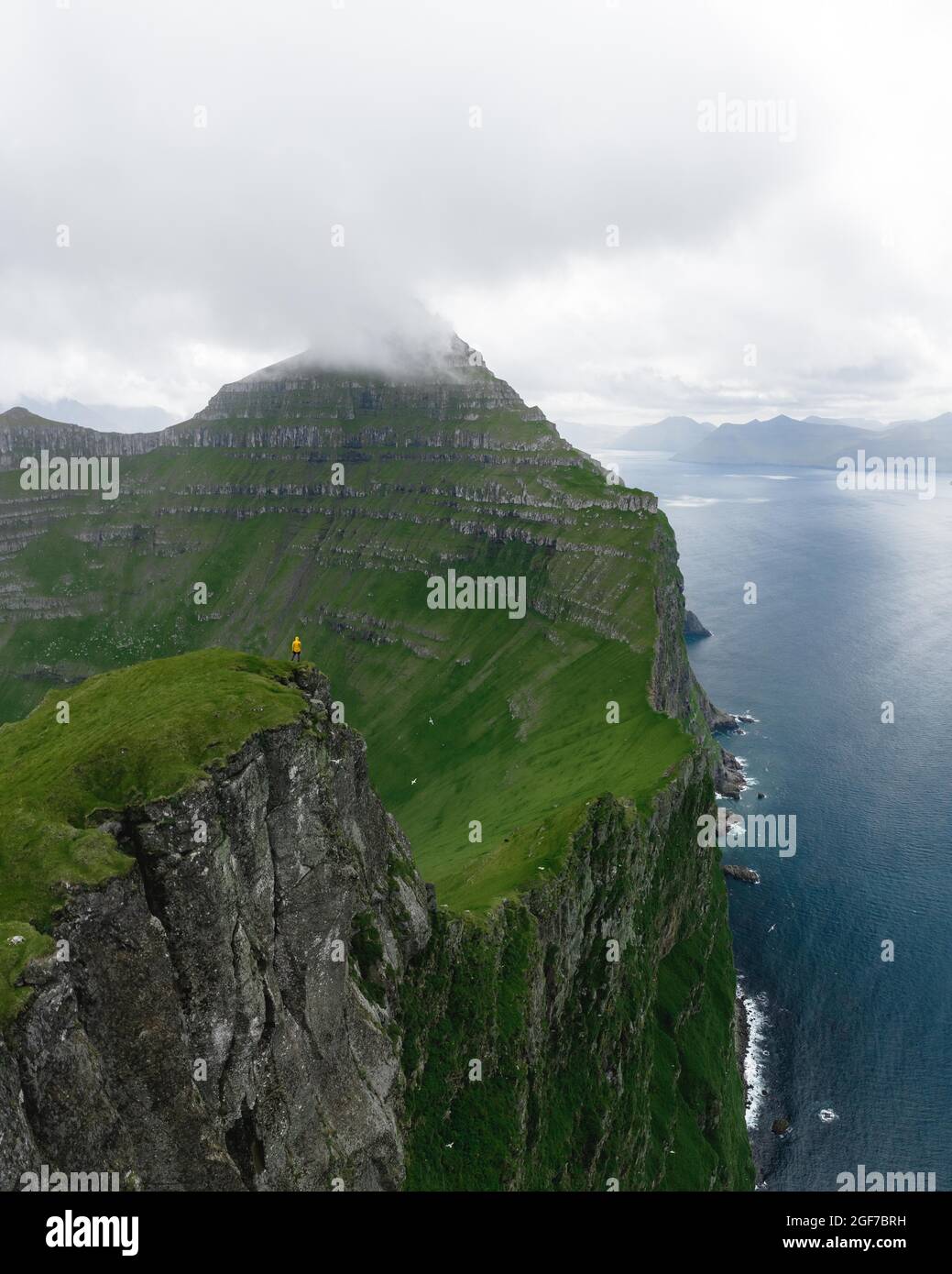 Luftaufnahme, Person, die auf hohen Klippen steht, markante Berge im Hintergrund, Kalsoy, Faro-Inseln Stockfoto