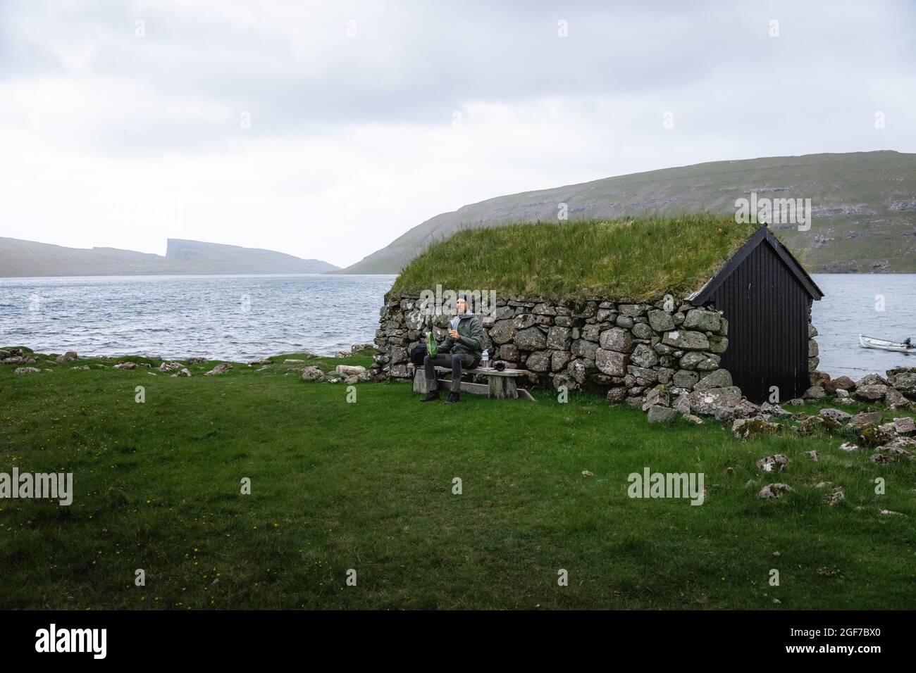 Wanderer essen Kekse auf einer Bank vor einer Steinhütte, Vagar, Färöer-Inseln Stockfoto