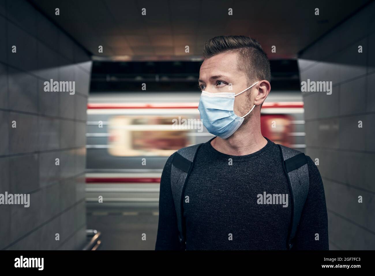 Mann mit Gesichtsmaske in U-Bahn-Station. Porträtieren Sie den Passagier in unscharfen Bewegungen gegen den Zug. Stockfoto