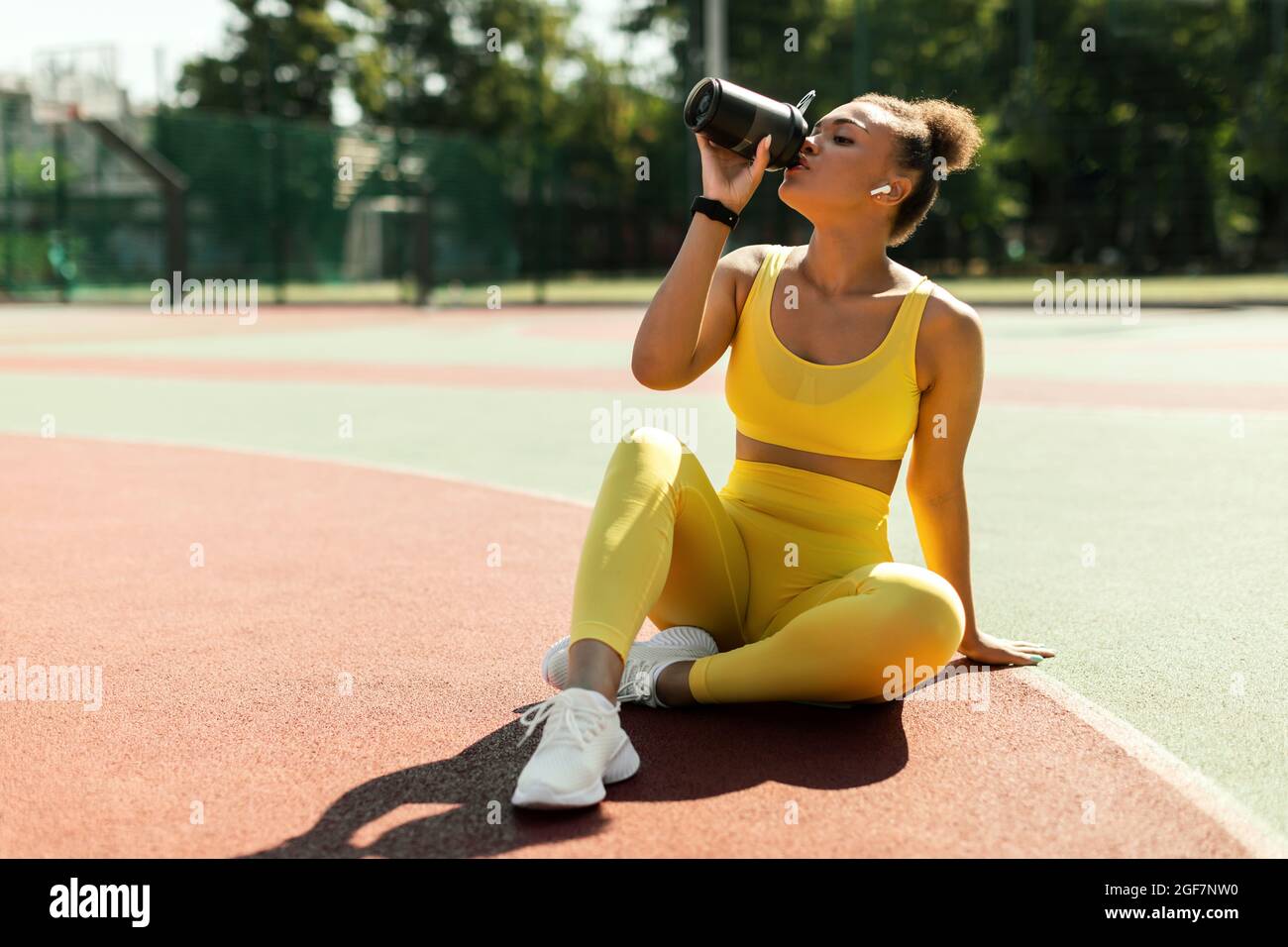 Porträt einer sportlichen schwarzen Frau in gelbem Sportswear-Trinkwasser Stockfoto